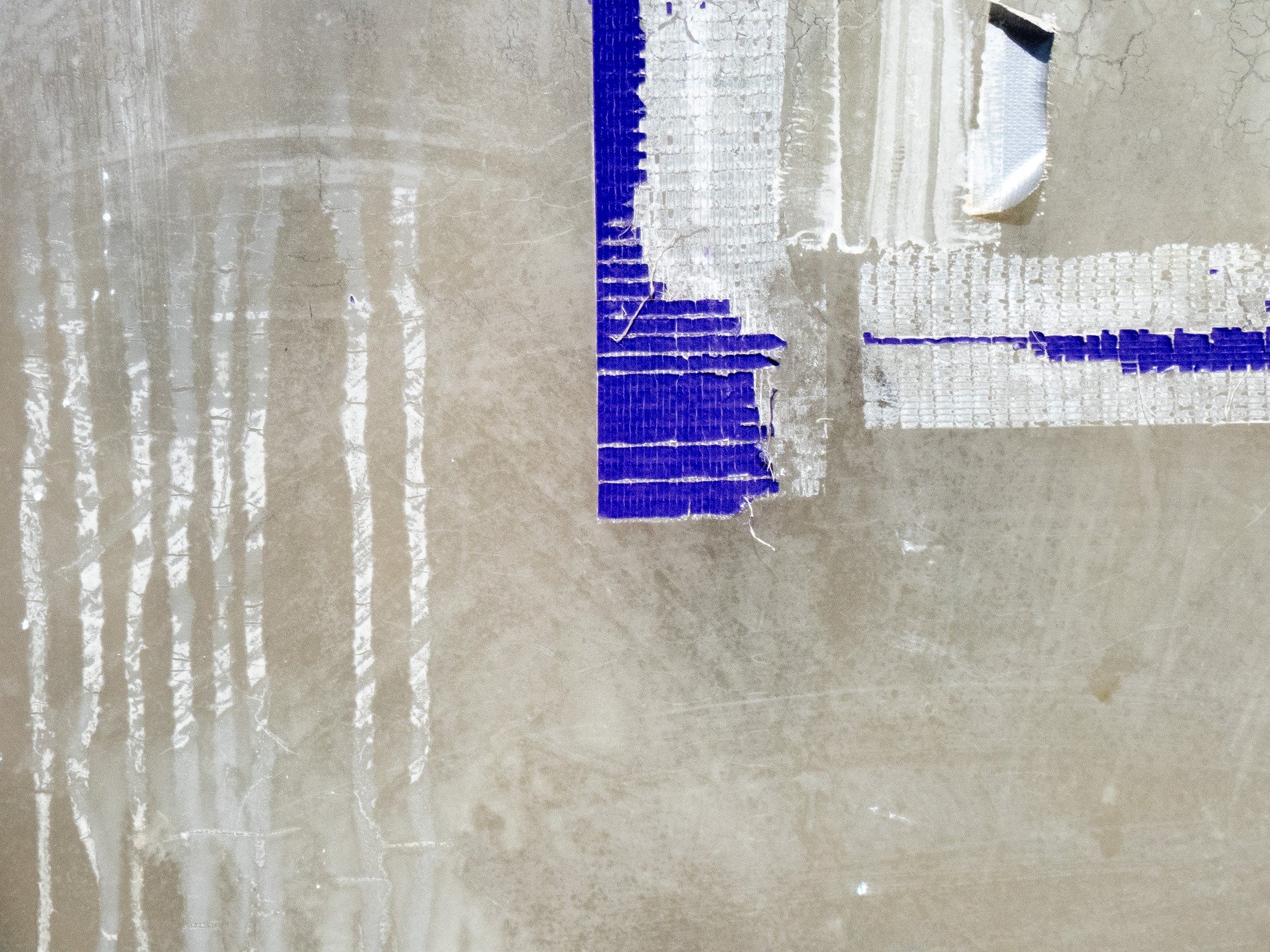 Adhesive residue on glass, grey background holds the grit, tape marks the pane