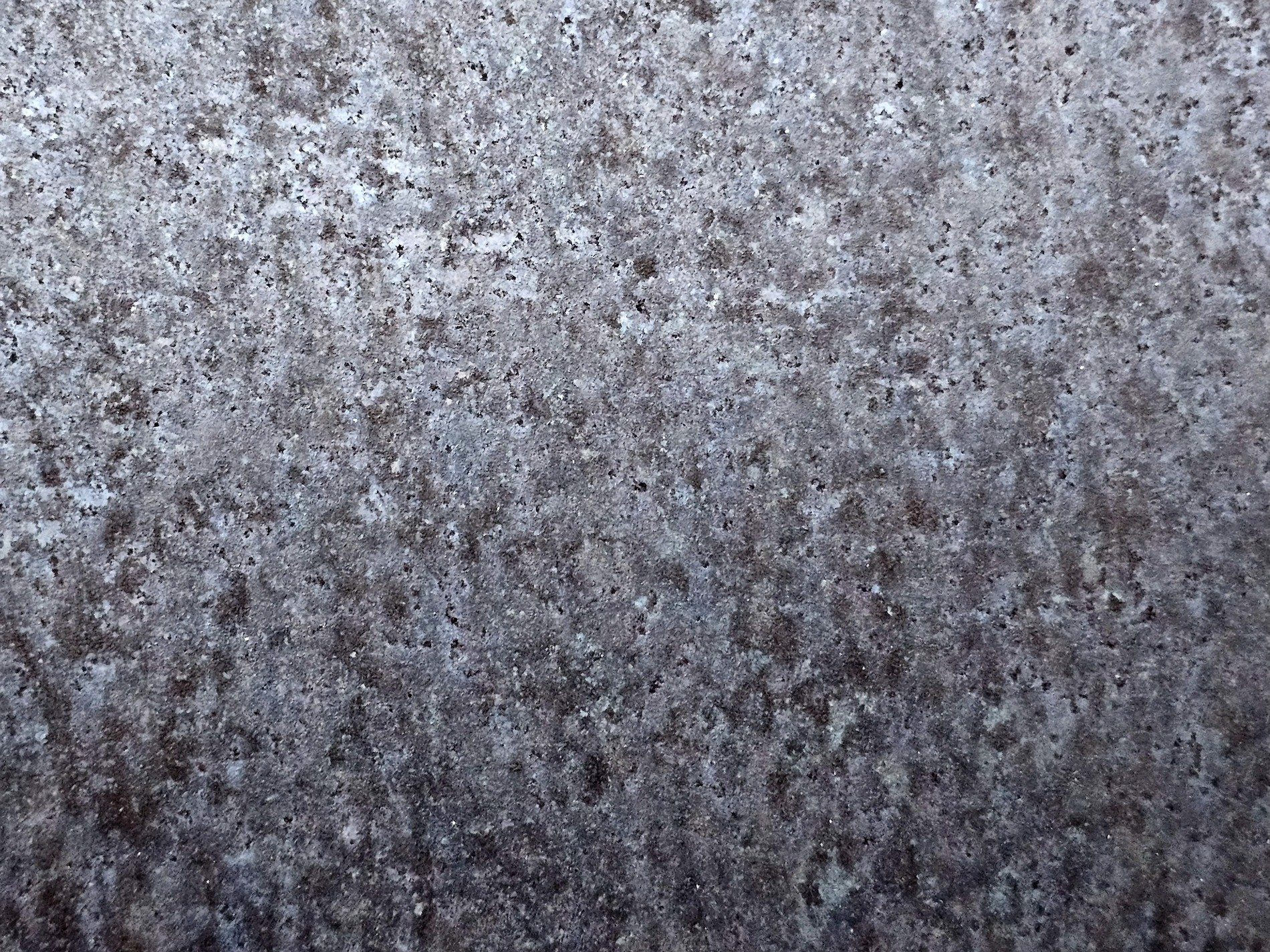 Grey stone grain holds light, dark specks scatter on the wall, silent texture speaks