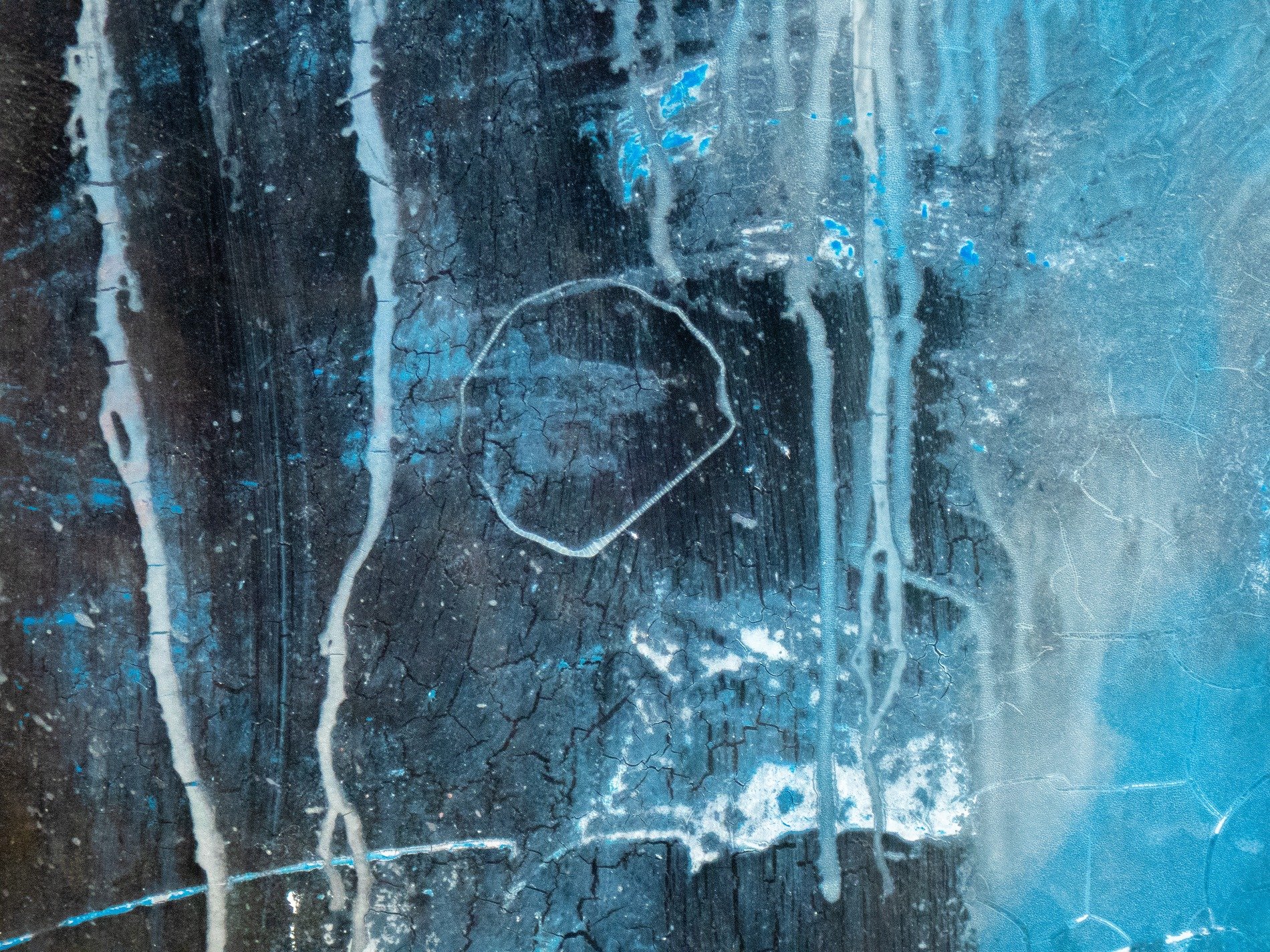 Blue flakes drift away, light catches the jagged edge, grit marks the clear field