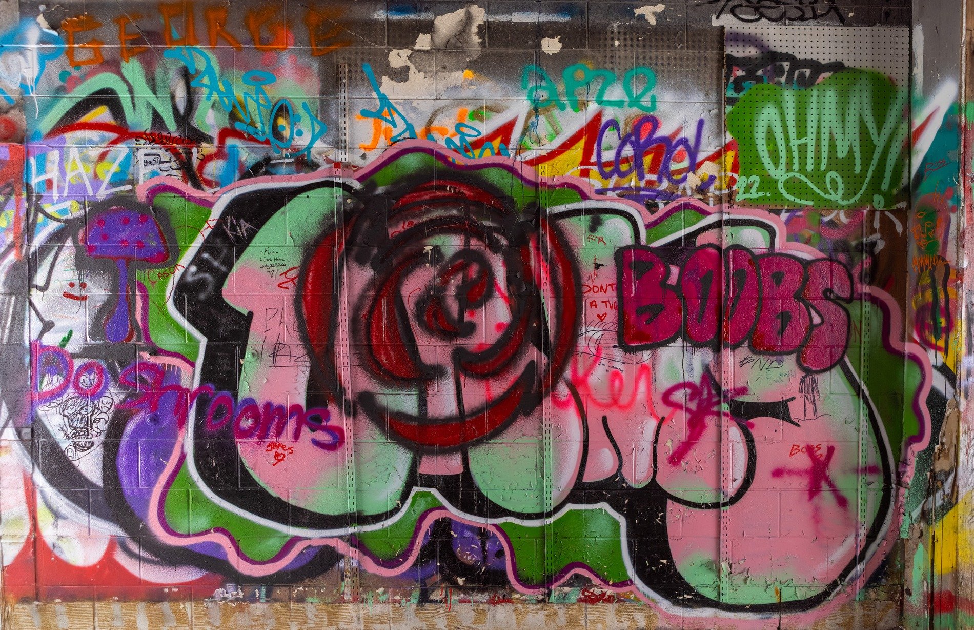 Blue graffiti on wood peg board, jagged letters meet the grain, holes mark the pattern