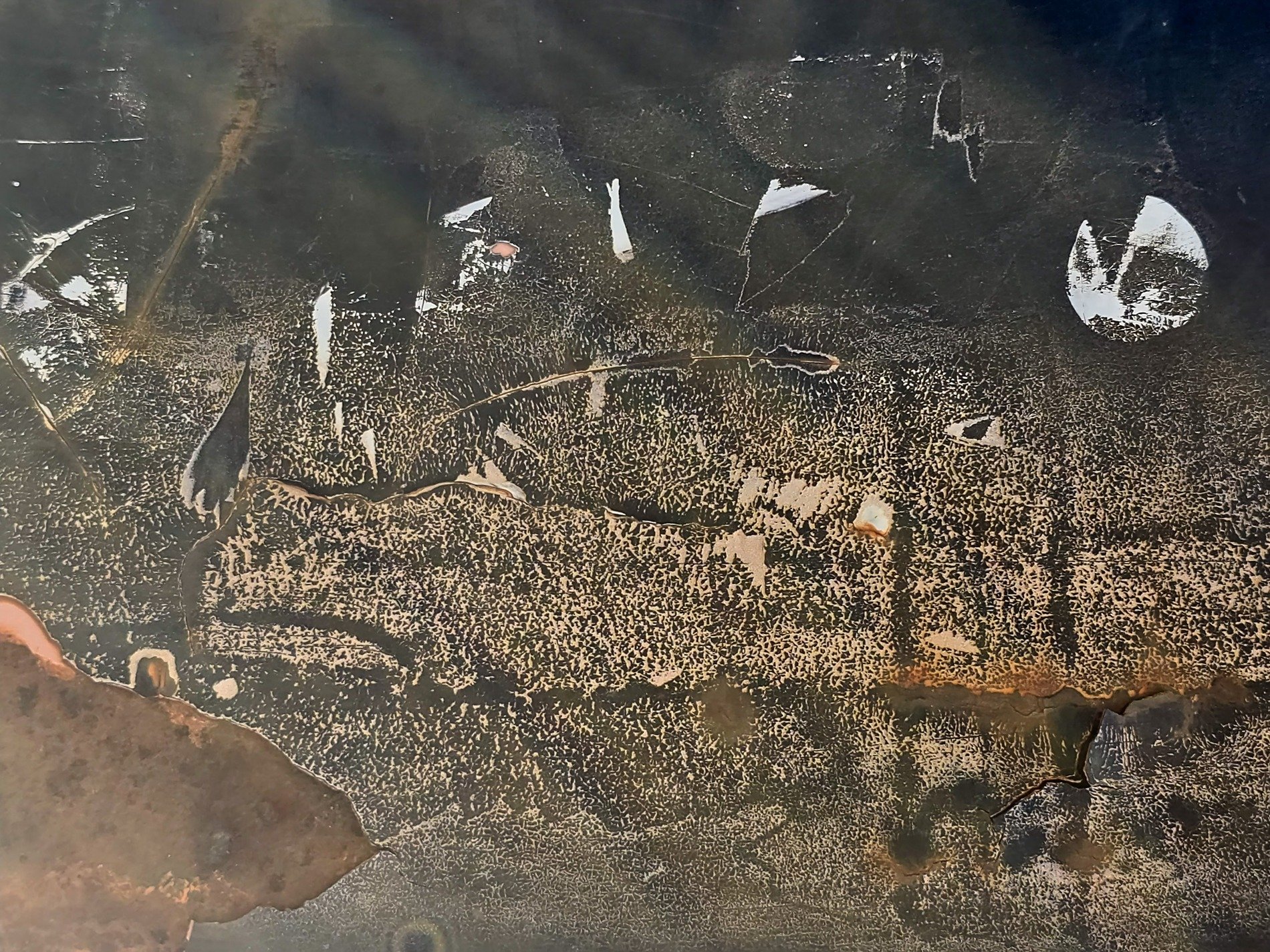 Dark metal decays, orange rust eats through the paint, white scars mark the surface