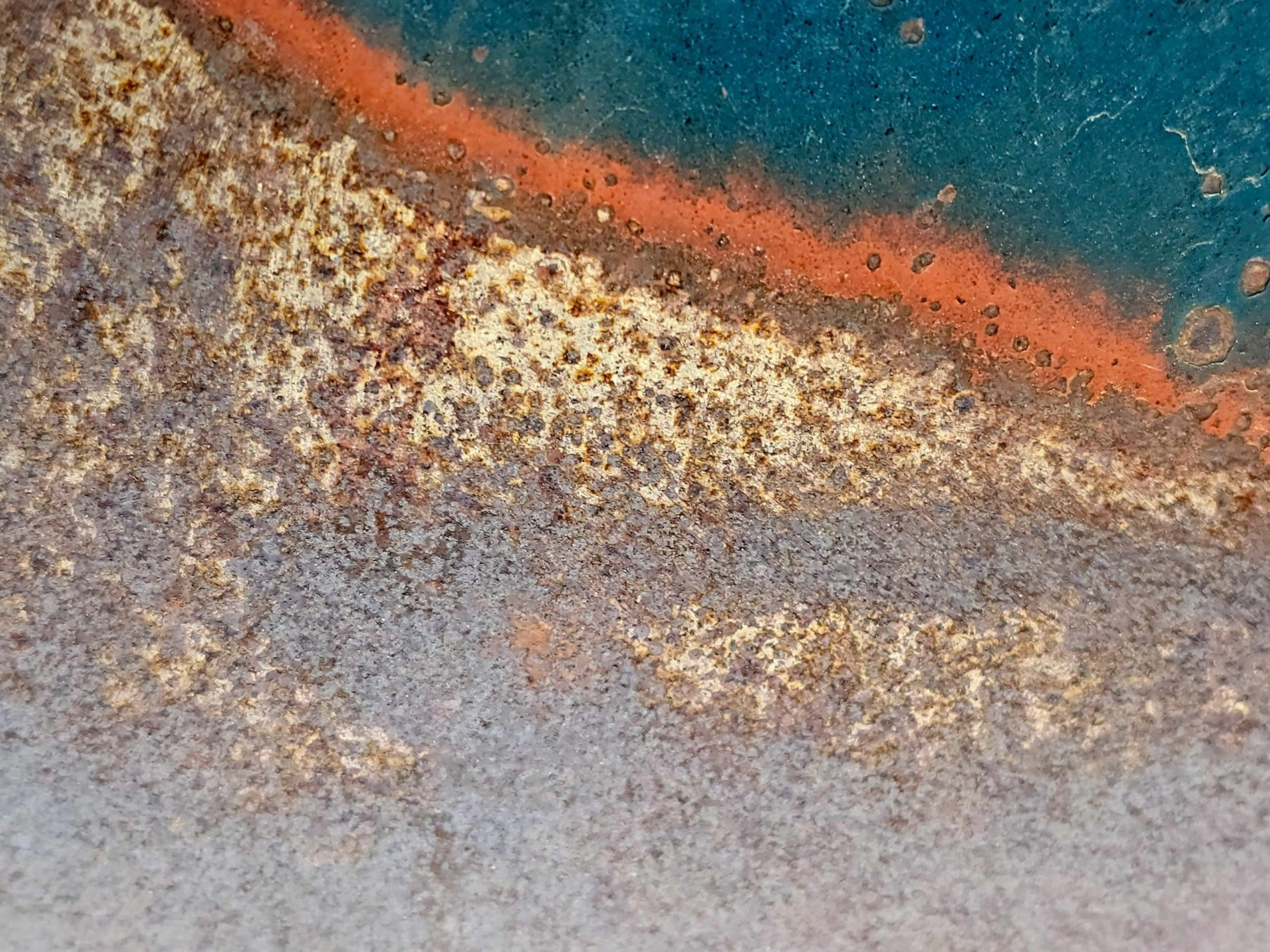 Blue paint holds the edge, orange rust spots mark the steel, grit marks the finish