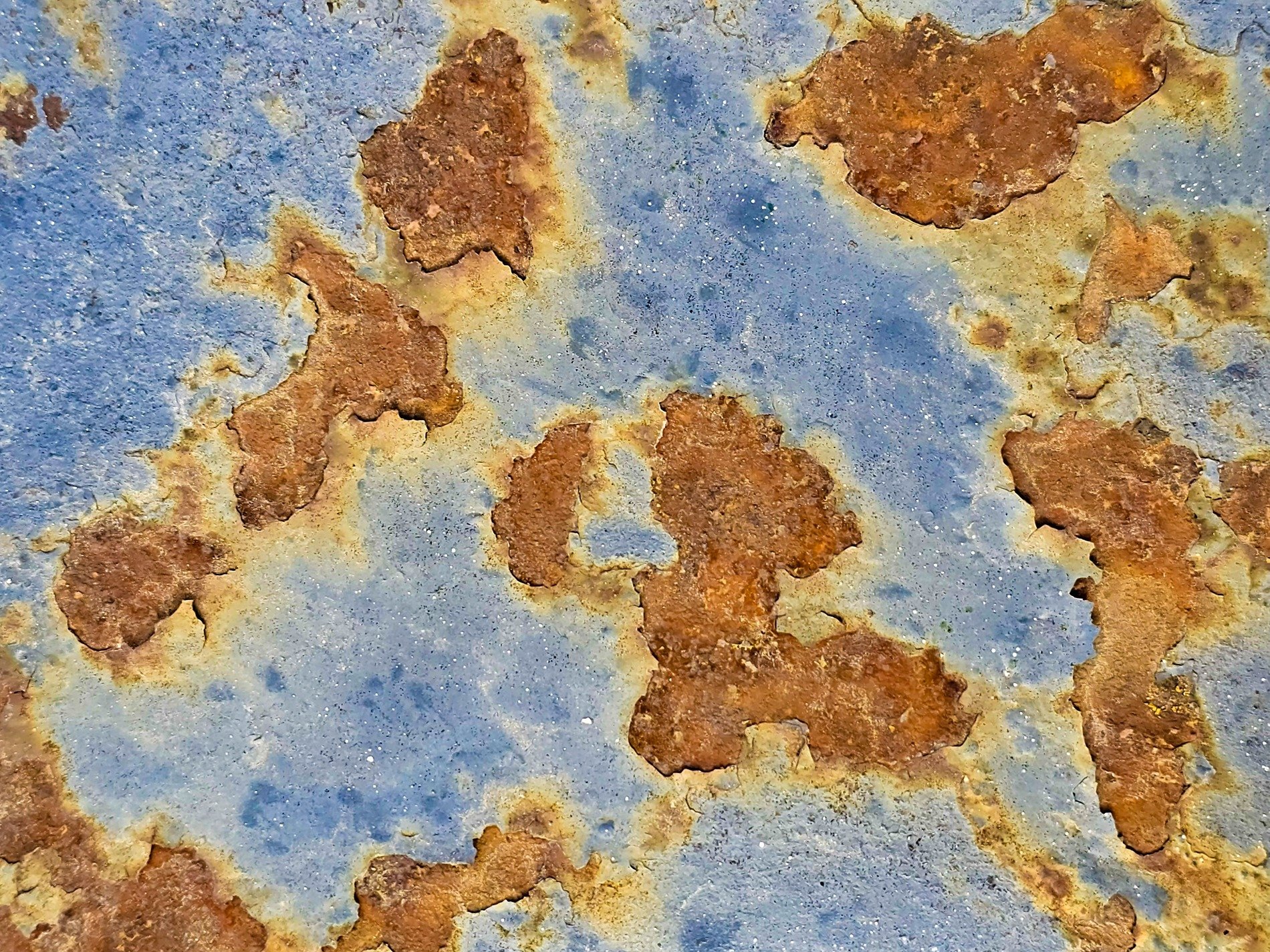 Blue paint flakes away, orange rust blooms on the steel, time claims the surface