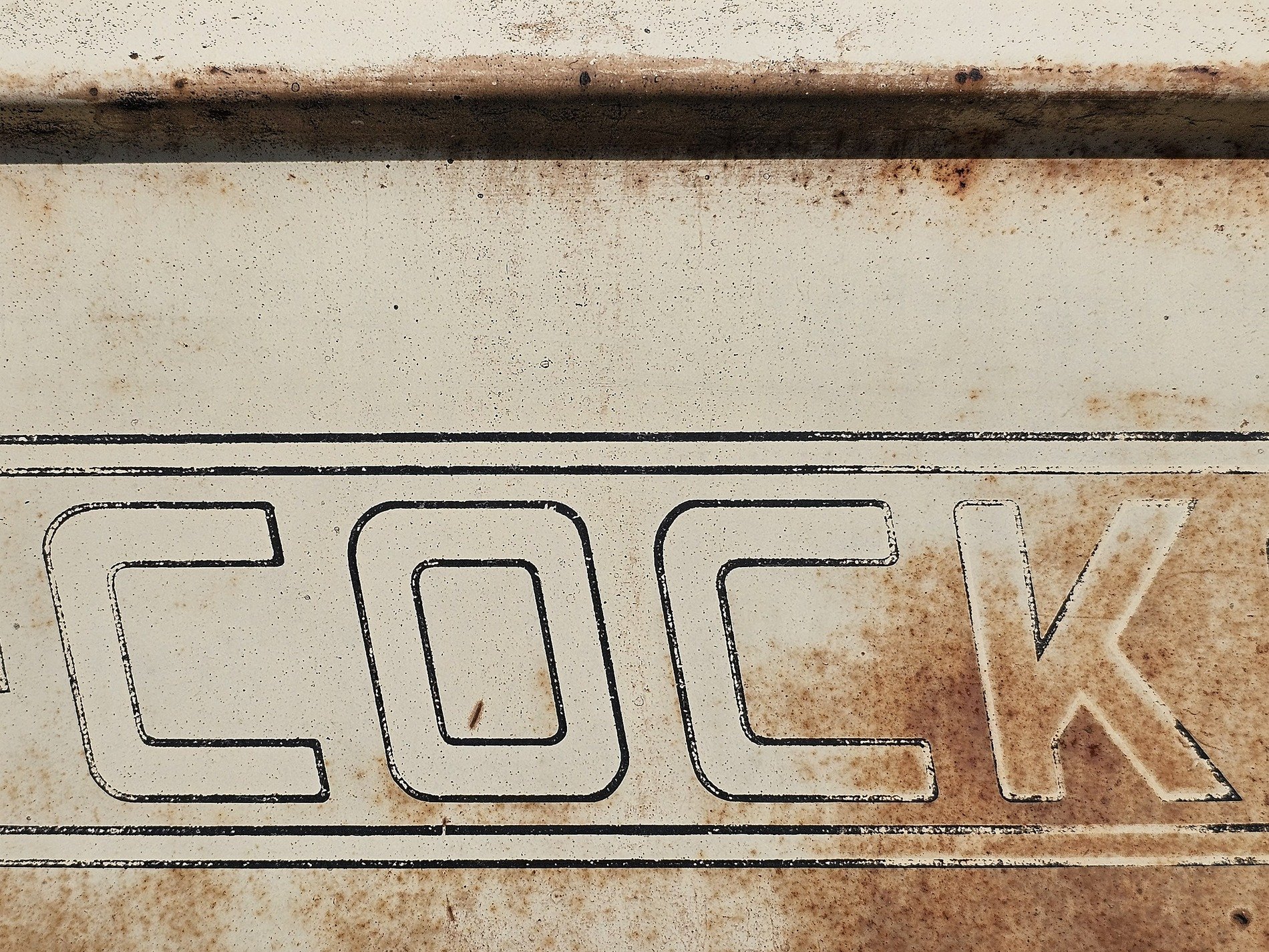 Bold letters on white, rust specks mark the metal skin, paint wears thin and old