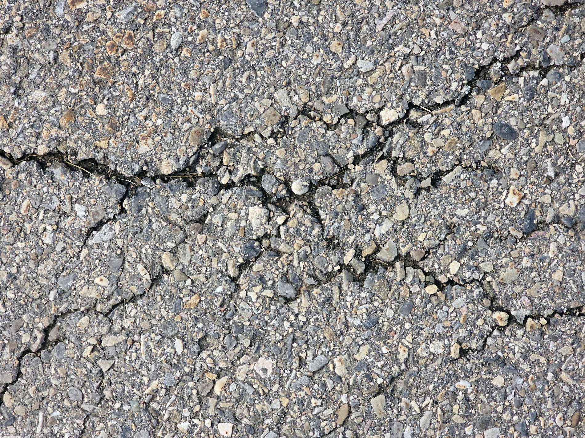 Dark cracks split the path, rough stones on the dry asphalt, grit holds the broken