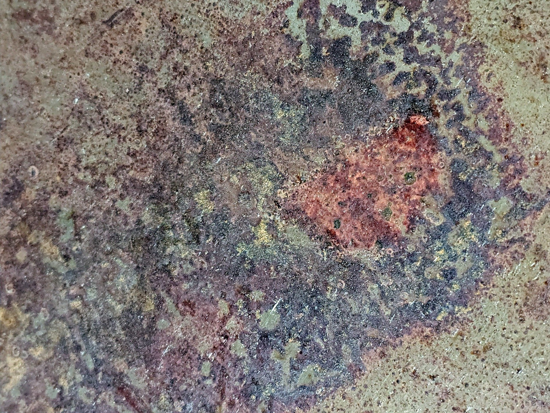 Dark paint holds the grit, brown rust blooms on the metal, time wears down the skin