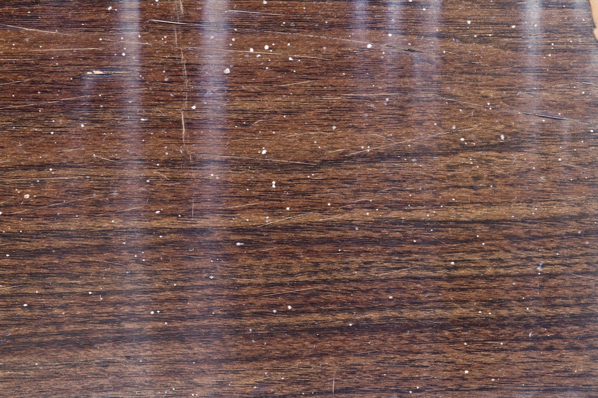 Dark wood shows the grain, white spots scatter on the brown, grit meets the finish