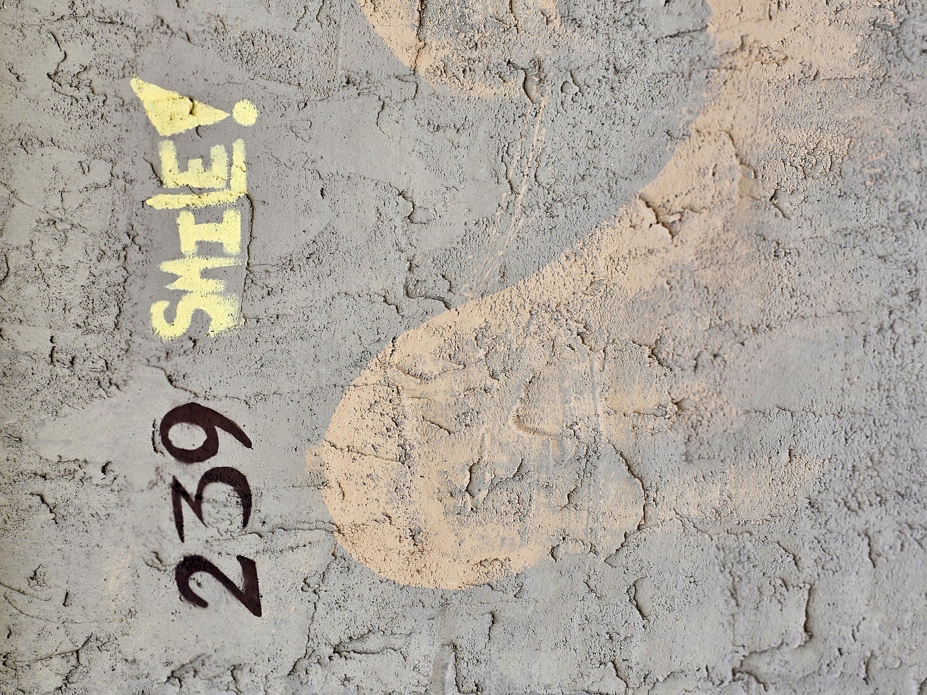 Cracks on grey stucco, yellow letters urge a grin, numbers mark the space