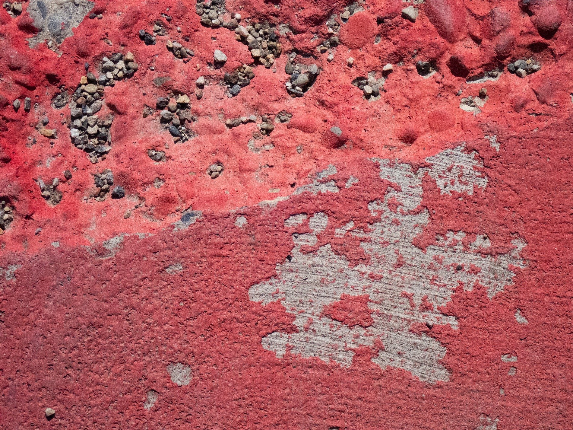 Red paint flakes away, grey stone hides beneath the crust, gravel finds its place