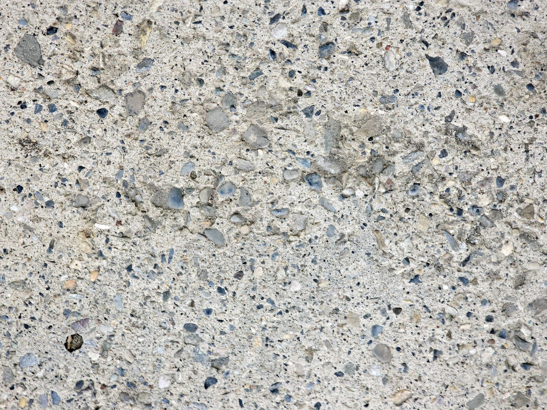 Grey stones in the mix, rough concrete holds the pebbles, grit fills the surface