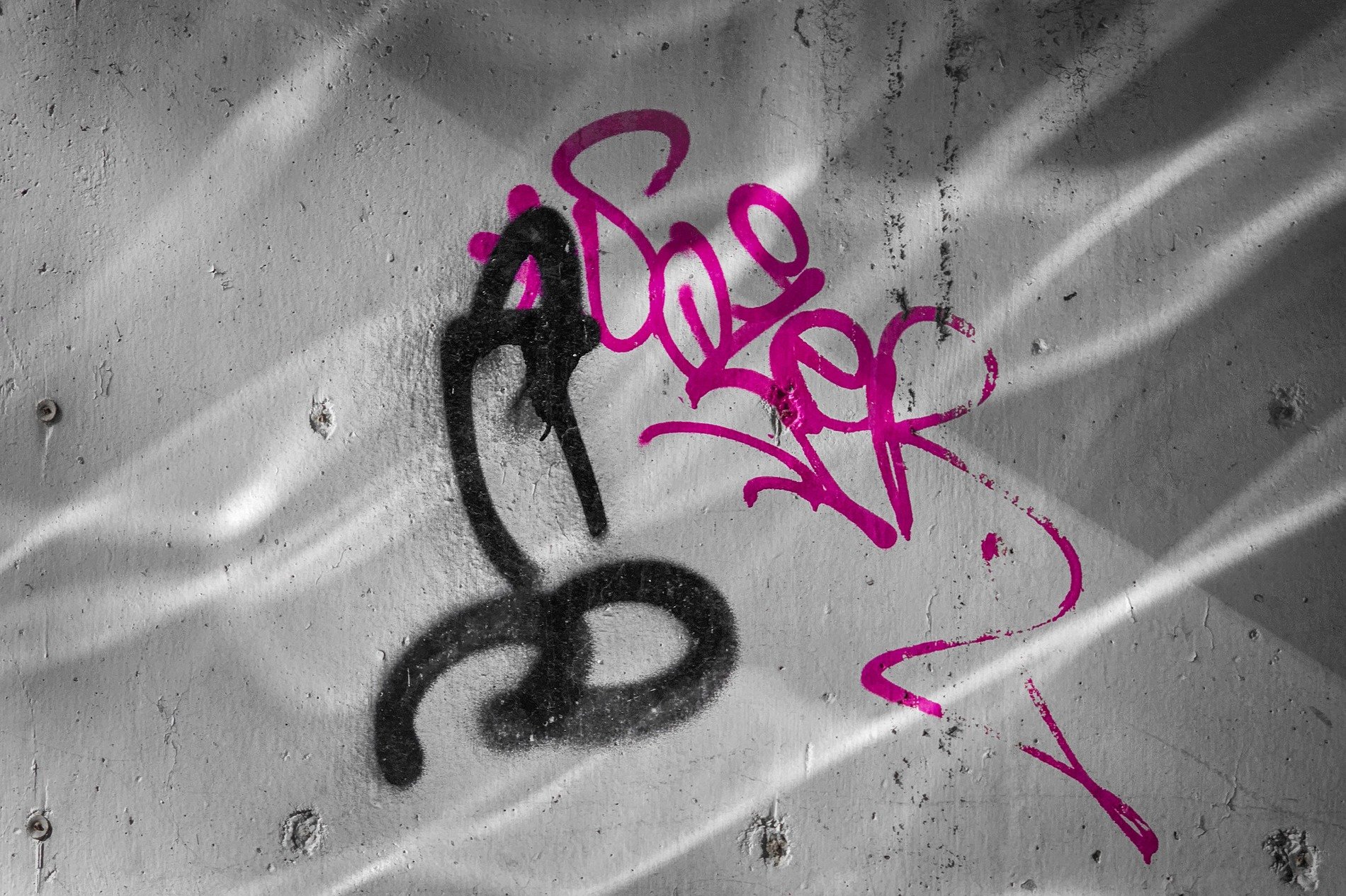 Pink paint on the wall, black ink traces rough concrete, shadows mask the grit