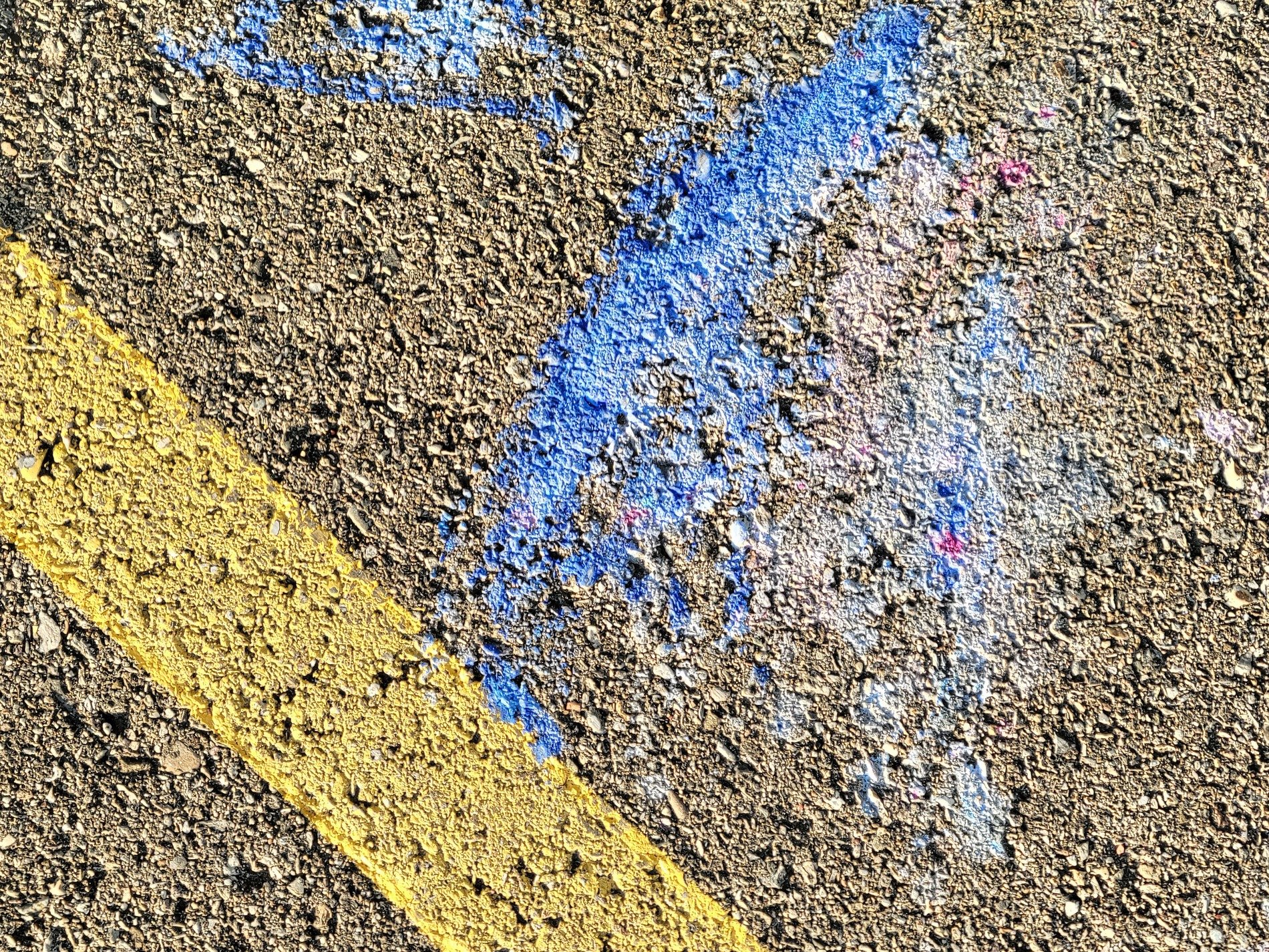 Purple chalk on the road, blue and yellow marks on asphalt, grit meets the light