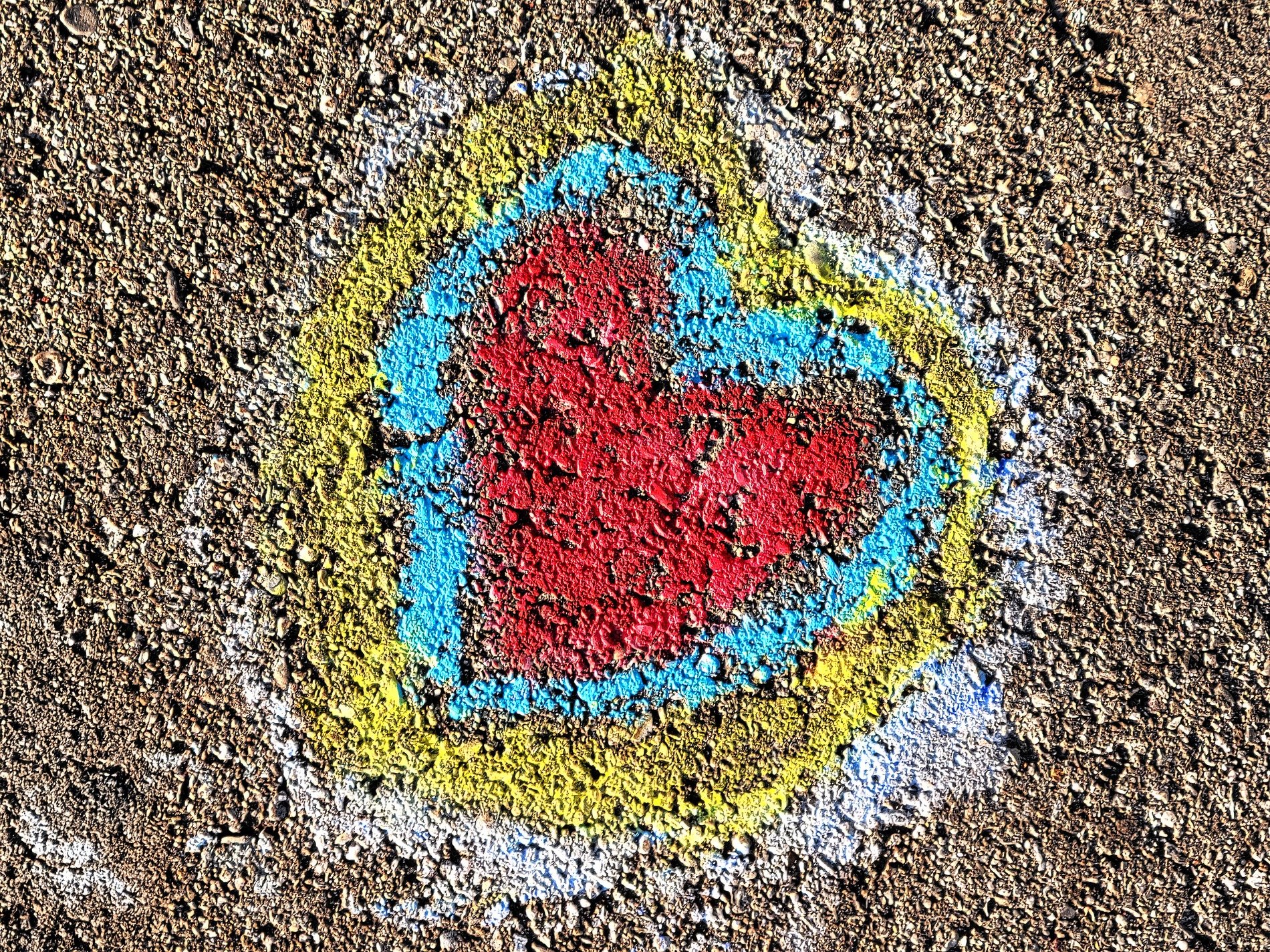 Red heart on the ground, blue and yellow trace the edge, chalk meets heavy grit
