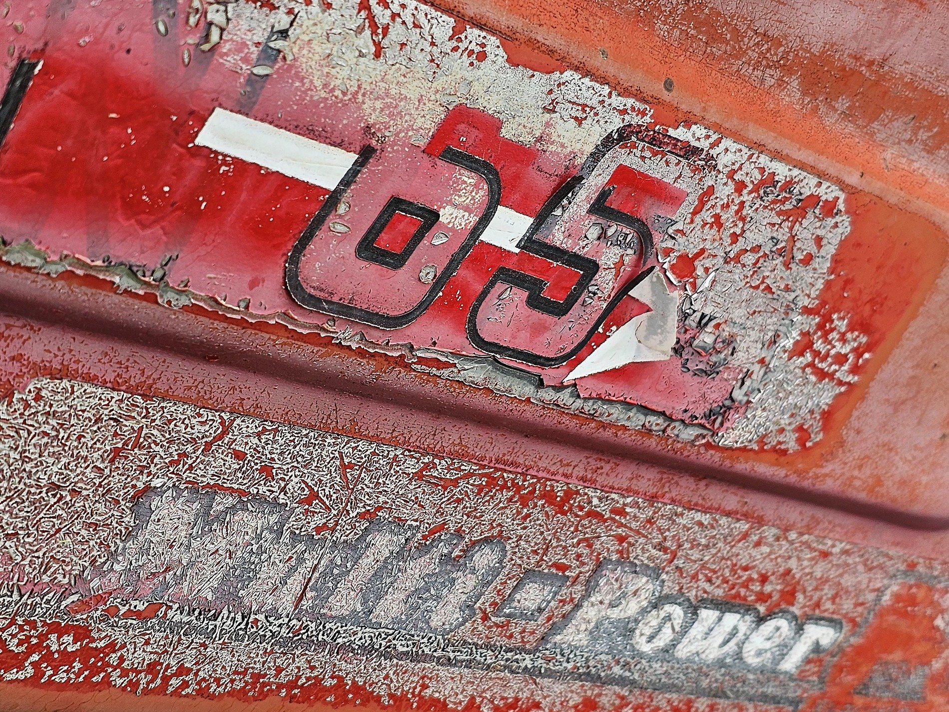 Red paint peels away, faded numbers mark the steel, rust breaks through the word