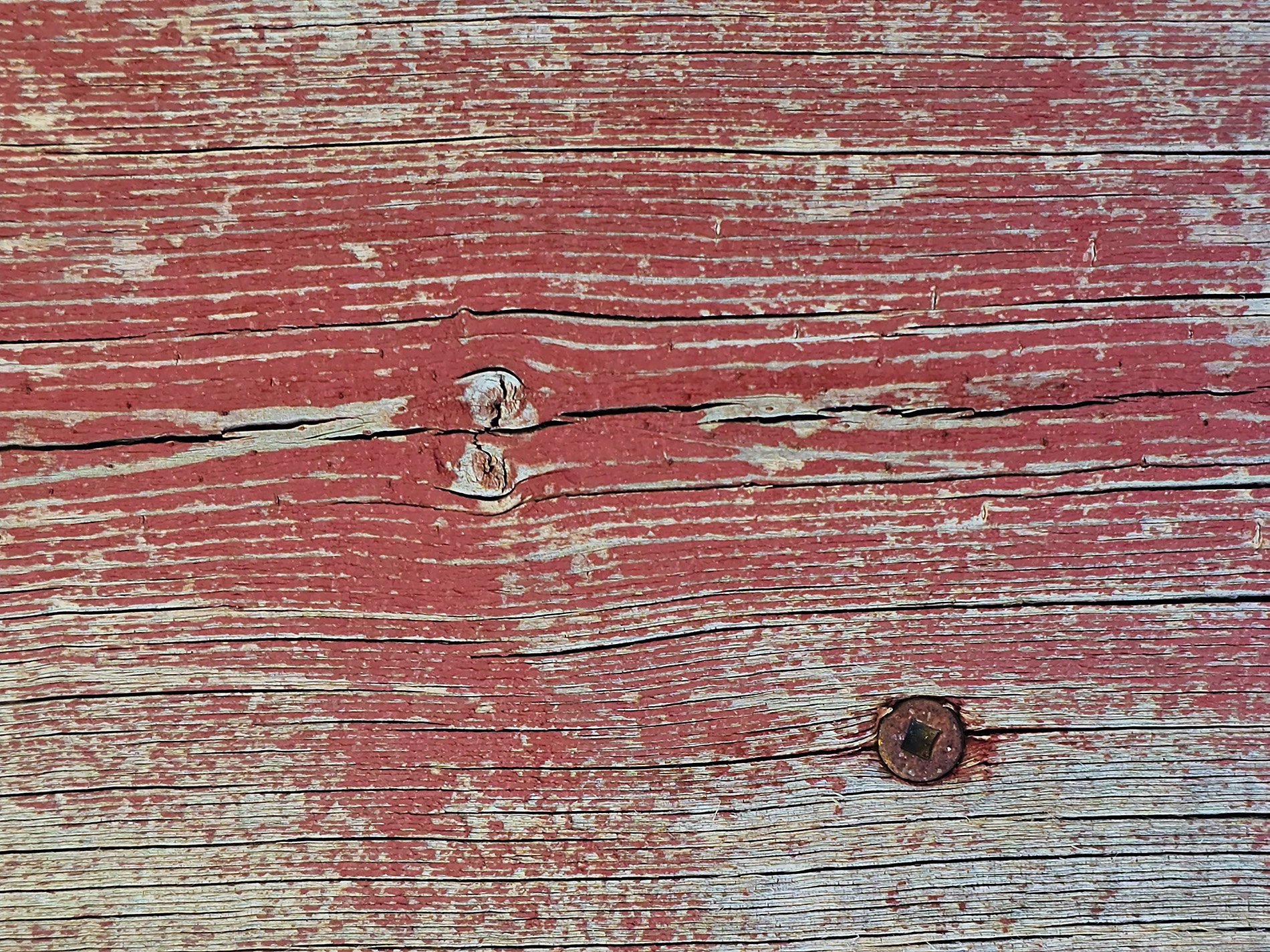 Red paint peels away, knots and cracks trace the old grain, iron holds the wood.