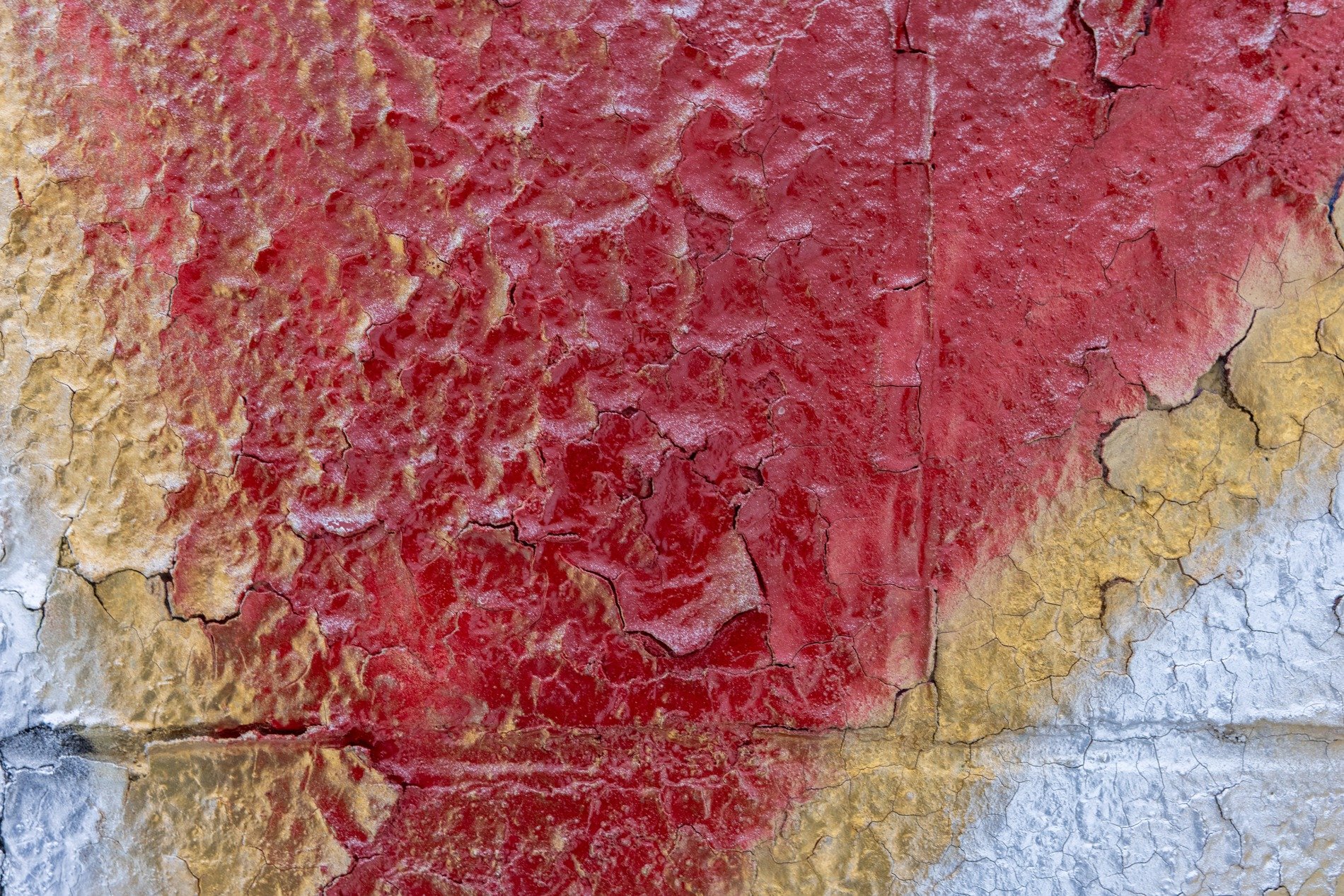 Red paint scales away, yellow cracks on faded white, grit meets the finish