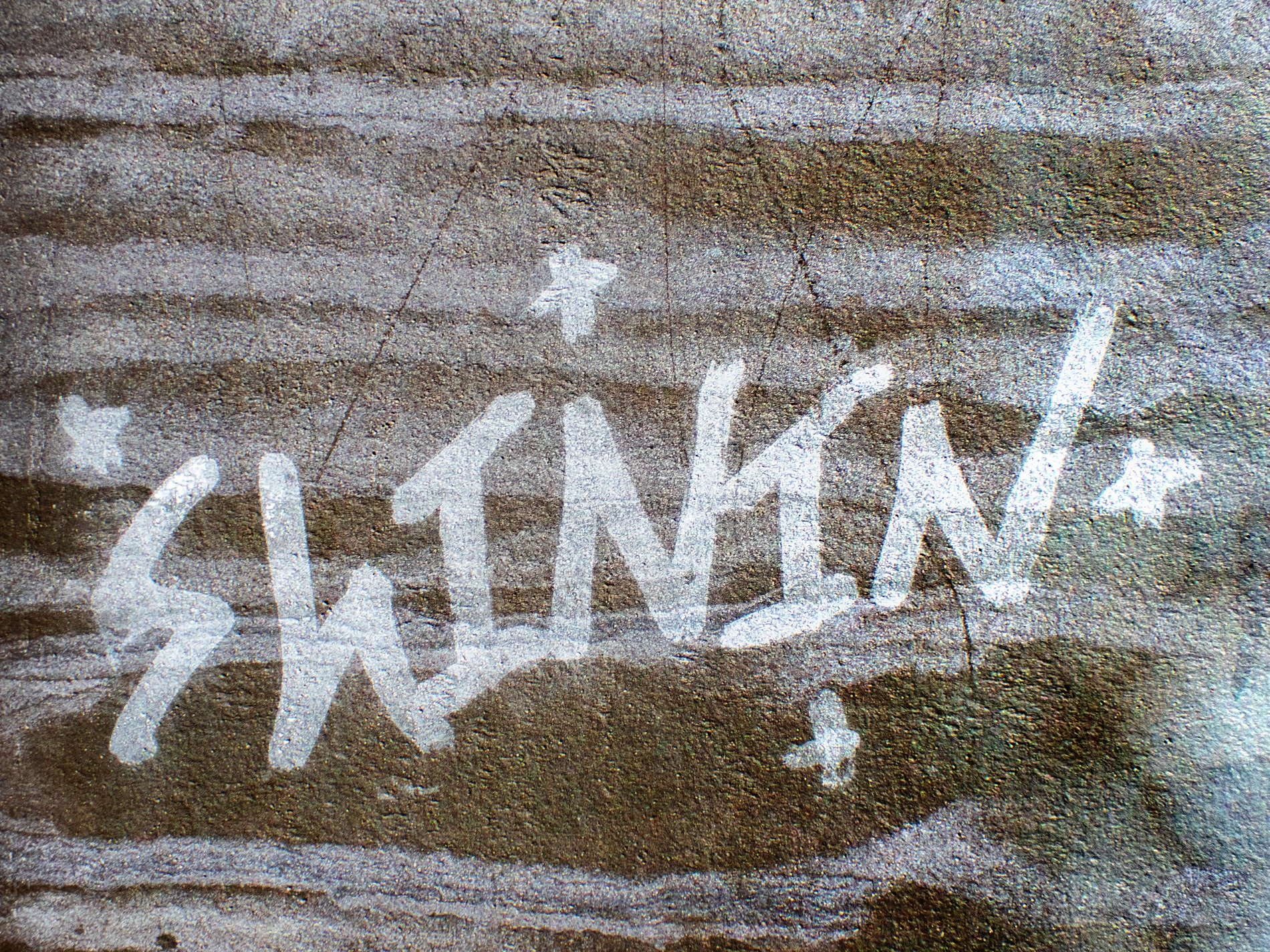 Silver paint on stone, bright flakes meet the grey grit, light catches the skin