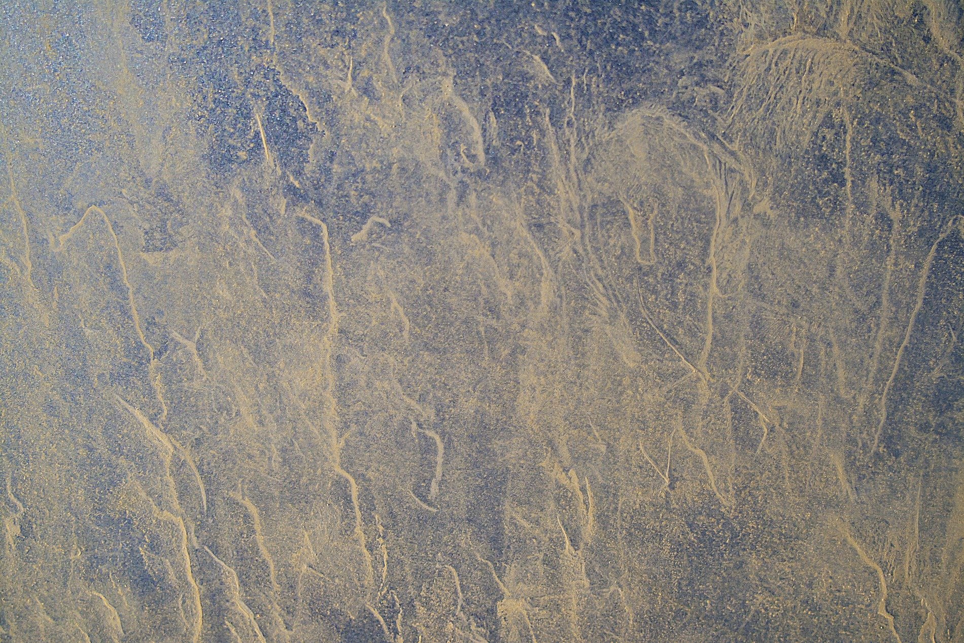 Silver skin has pits, jagged lines trace the metal, light catches the grit