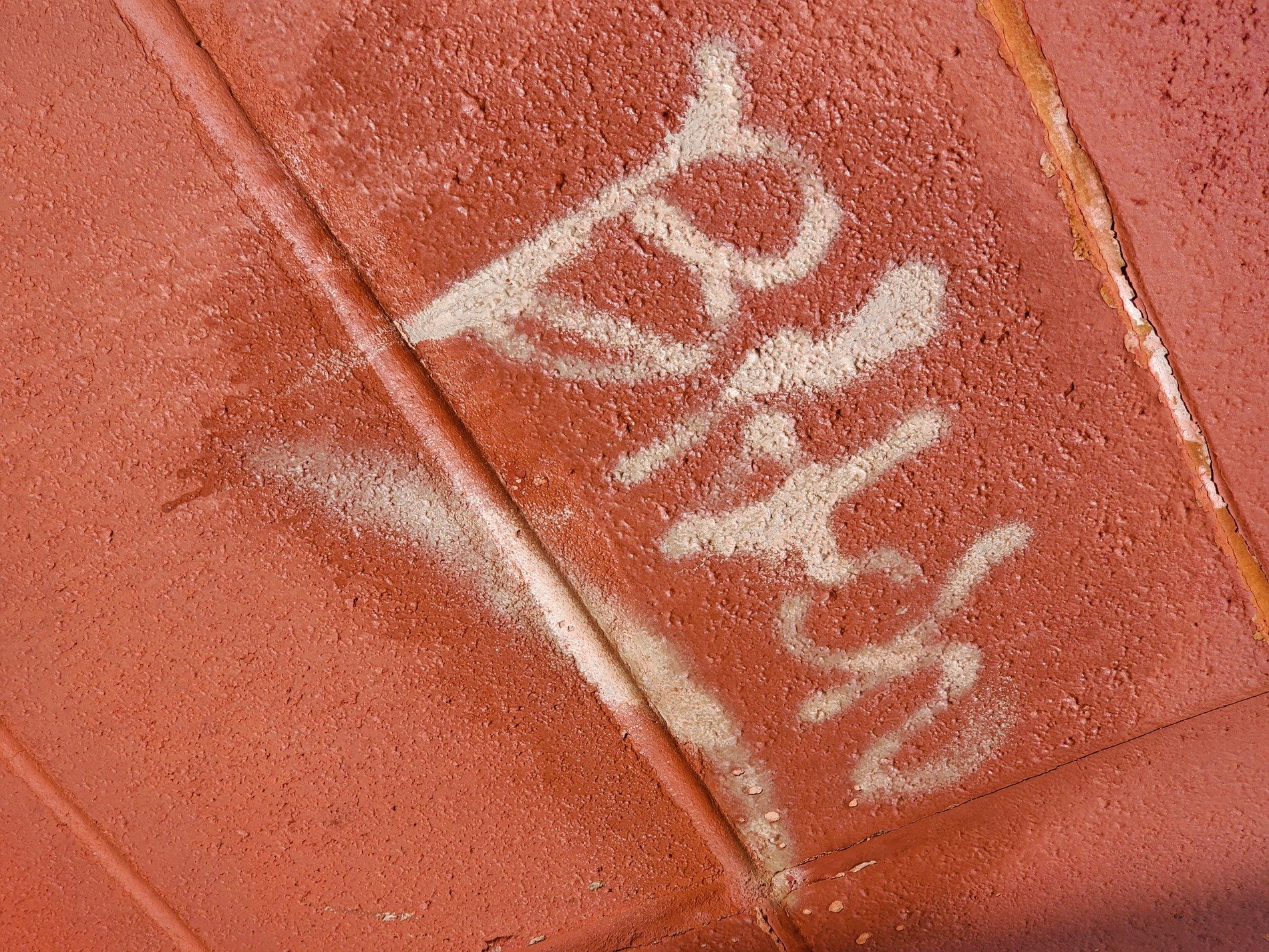 White paint marks the red, rough stucco grips the letters, seams cut through the frame
