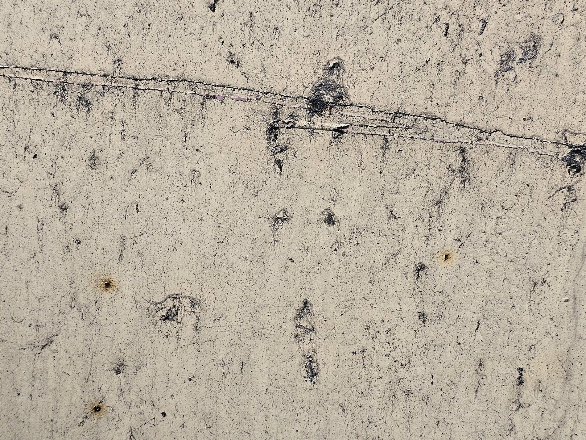 Tan pits on the wall, black streaks mark the fading paint, grit meets the rough board