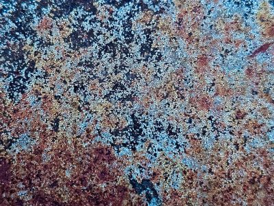 Blue cracks on the steel, orange rust blooms in the dark, time paints a mosaic