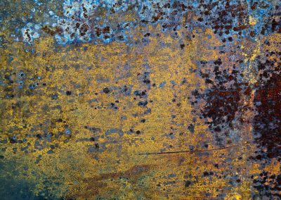 Blue fields in the light, orange rust edges the frame, grit holds the shoreline