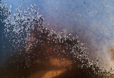 Blue fields meet the dark, white specks line the rusted edge, grit marks the shoreline