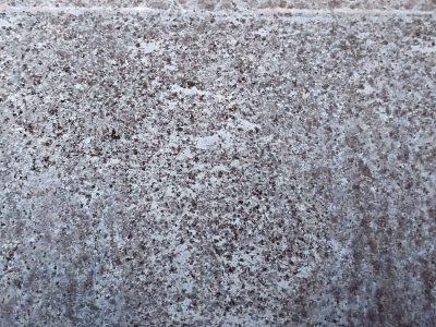 Speckled surface grey, purple grains embedded deep, cold stone stands its ground