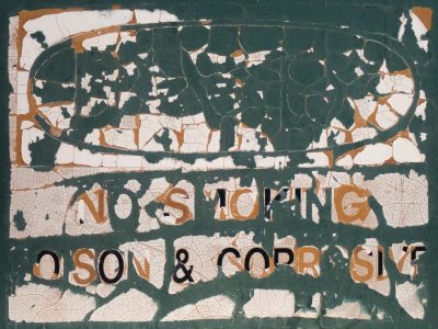 Green sign flakes away, white paint cracks like desert mud, warnings fade from sight