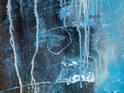 Blue flakes drift away, light catches the jagged edge, grit marks the clear field