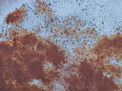 Blue layers peel back, white flakes meet the grey below, grit holds the surface