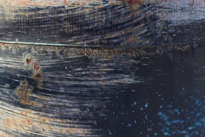 Blue paint flakes away, orange rust blooms on the plate, time leaves a thick mark