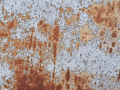 White paint flakes away, orange rust maps the surface, iron meets the air