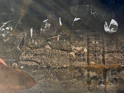 Dark metal decays, orange rust eats through the paint, white scars mark the surface