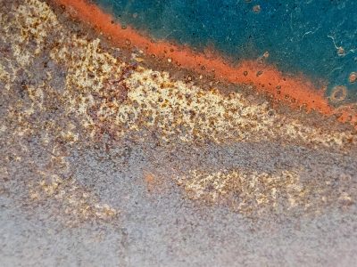 Blue paint holds the edge, orange rust spots mark the steel, grit marks the finish