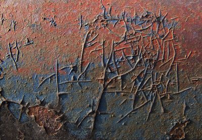Blue paint meets the rust, orange veins bleed on the steel, grit holds the pattern
