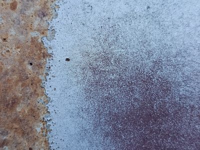 Blue paint scales off, orange rust meets the cold steel, grit holds the shoreline