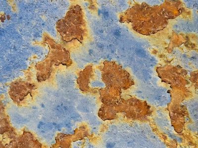 Blue paint flakes away, orange rust blooms on the steel, time claims the surface