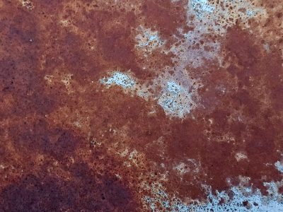 Blue skin flakes away, orange oxidation claims the surface, grit holds the decay