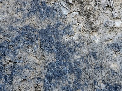 Grey stone wears its age, blue stains bleed through weathered crust, layers fall to dust