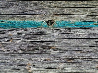 Weathered grain runs long, teal paint marks a wooden knot, aged grey timber rests
