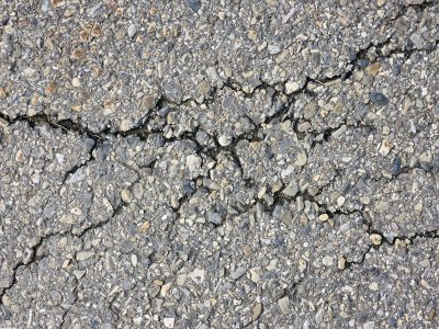 Dark cracks split the path, rough stones on the dry asphalt, grit holds the broken