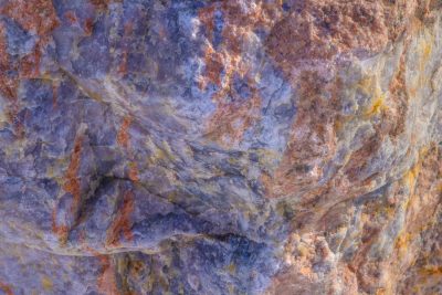 Dark grains flow through deep, orange spots mark the surface, grit holds the pattern