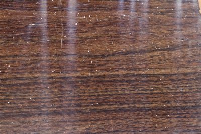 Dark wood shows the grain, white spots scatter on the brown, grit meets the finish