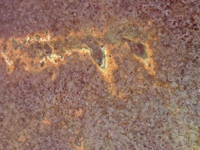 Red dust coats the steel, orange scars bloom on the surface, iron turns to earth