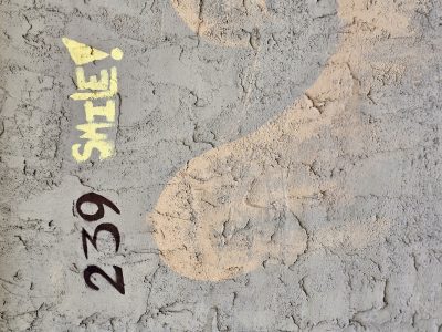 Cracks on grey stucco, yellow letters urge a grin, numbers mark the space