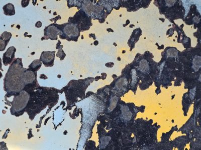 Grey paint peels away, orange rust spots mark the plate, grit holds the surface