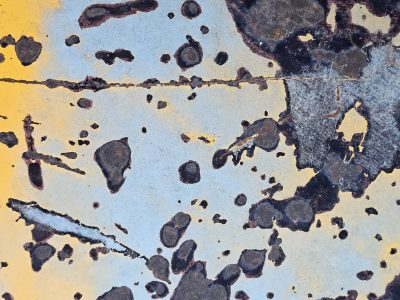 Blue paint starts to peel, dark rust blooms across the steel, yellow fades from sight