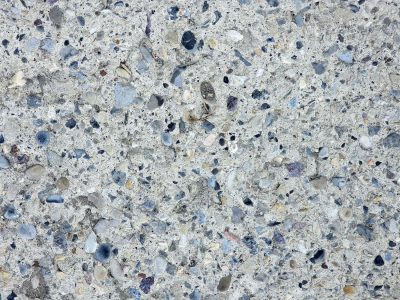 Grey stones in the mix, rough concrete holds the grit, time wears the finish