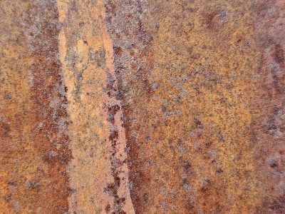 Orange dust on steel, rough pits scar the heavy plate, rust claims the surface